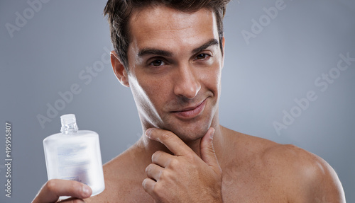 He always looks and smells great. Studio shot of a handsome young man applying aftershave to his face. photo