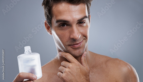 He always looks and smells great. Studio shot of a handsome young man applying aftershave to his face.