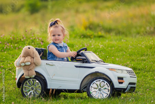 little girl rides on a children's car on a green lawn