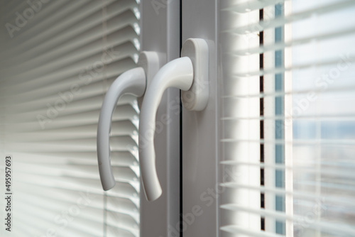 Handles of closed white plastic window with blinds.