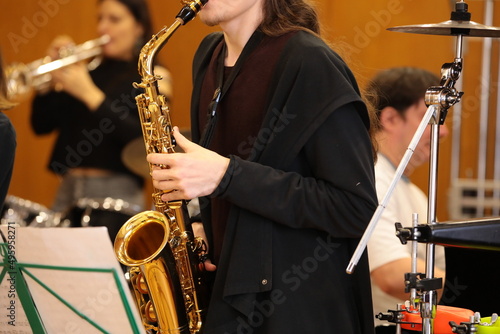 A person with a golden saxophone playing a concert on stage with drums and trumpet in a youth jazz band musician close up