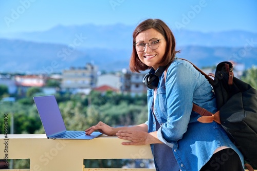 Portrait of beautiful woman 40s age with backpack laptop headphones, outdoor.