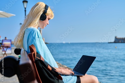 Young woman relaxing in headphones with a laptop on the seashore