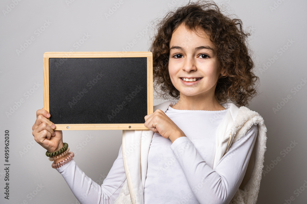 One small caucasian girl ten years old with curly hair front view portrait close up standing in front of white background looking to the camera hold board for text copy space One small caucasian girl ten years old with curly hair front view portrait close up standing in front of white background looking to the camera hold board for text copy space