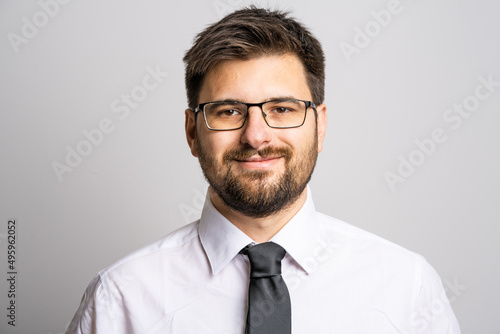 Portrait of one adult caucasian man 30 years old with beard and eyeglasses businessman or doctor looking to the camera in front of white wall background wearing shirt confidence success concept