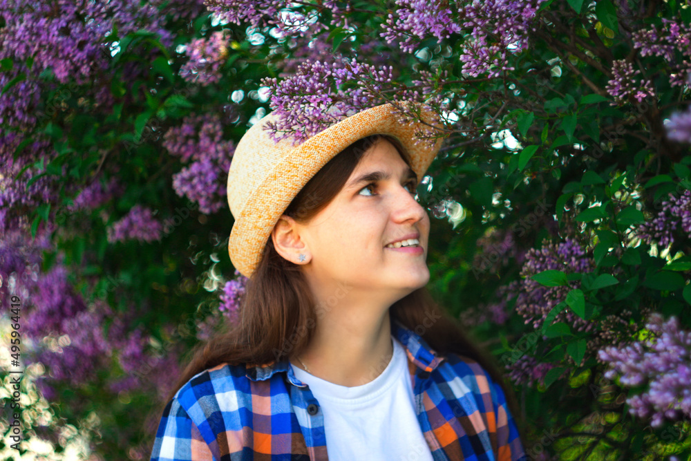 Spring girl. Defocus beautiful young woman near blooming spring tree. Bush lilac flowers. Youth, love, fashion, romantic and lifestyle concept. Girl in hat on nature background. Out of focus
