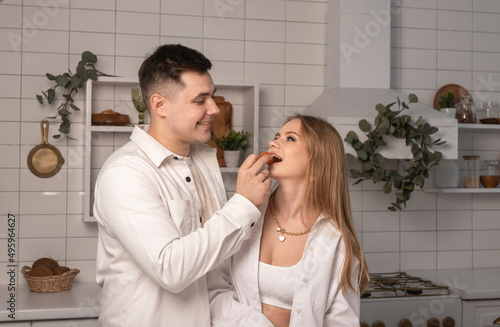 Man treating, feeding his wife. Husband putting fruit or candy into woman s mouth. Love couple having fun at home kitchen. High quality photo