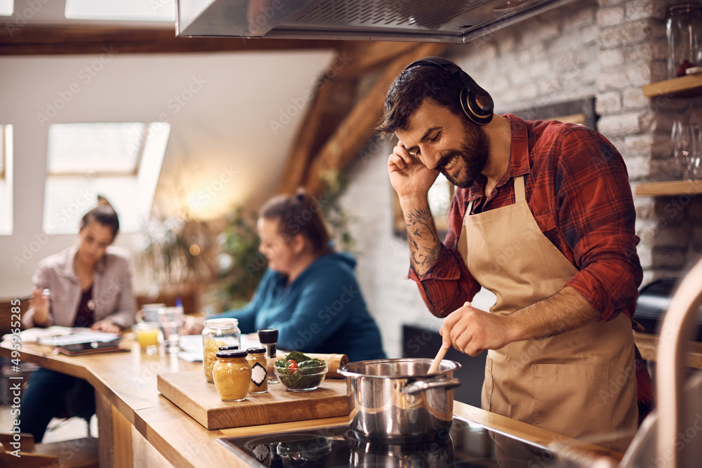 Happy man listens music over headphones while cooking at home.