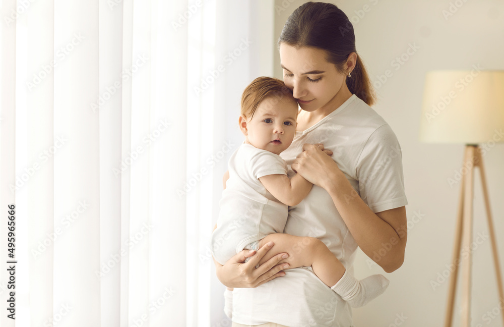 Happy mother together with her child at home. Beautiful young mom standing in a cozy room and holding her cute, sweet baby boy or girl in her arms. Family, love, care, motherhood, and nurture concepts Happy mother together with her child at home. Beautiful young mom standing in a cozy room and holding her cute, sweet baby boy or girl in her arms. Family, love, care, motherhood, and nurture concepts
