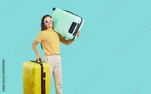 Smiling young woman with suitcases ready for summer tropical vacation go on tour. Happy female client with baggage prepare for holidays. Blue studio background. Travel and tourism concept. photo