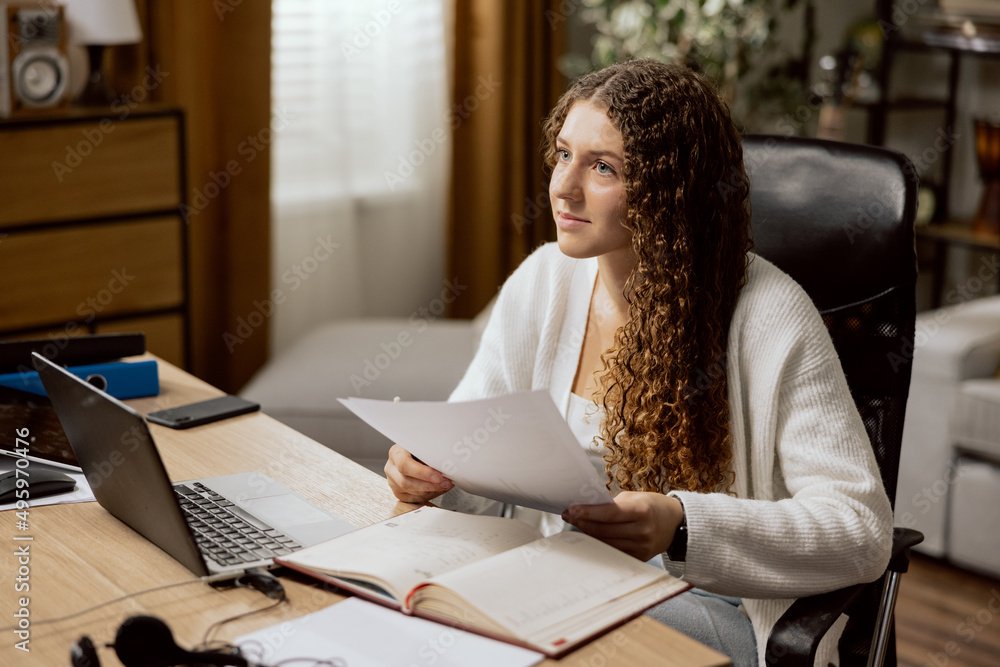 Φωτογραφία The girl teenager in a white sweater, studies online from home, sits in an offic