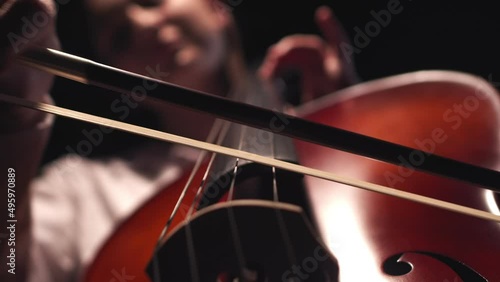 Musician leads bow along strings of cello playing classical music, closeup, front view. Musician performs playing classical melody on cello photo