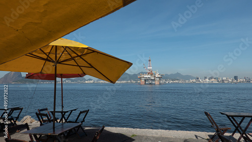 Gragoata neighborhood in Niteroi and its sidewalk by the sea with tables to enjoy the landscape with the silhouette of the city of Rio de Janeiro on the horizon and a sea oil platform. photo