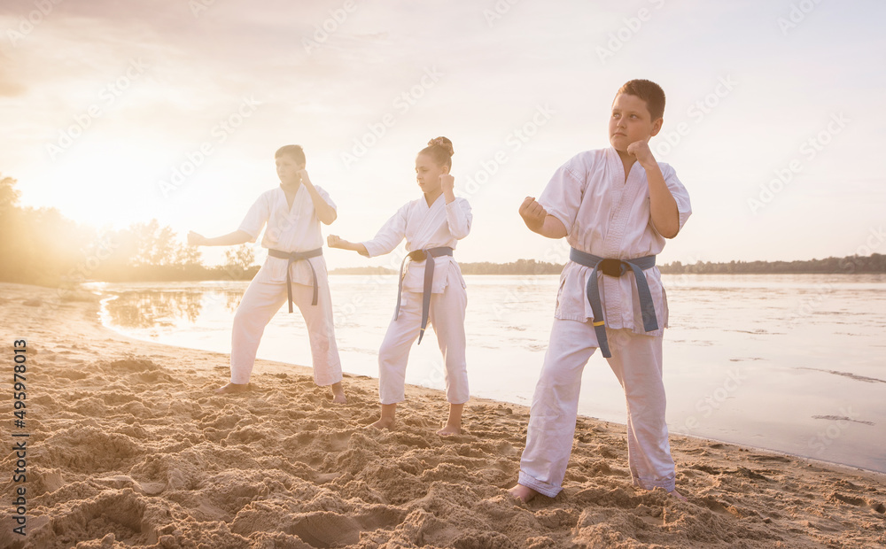 Children karate section training on beach sand near the river