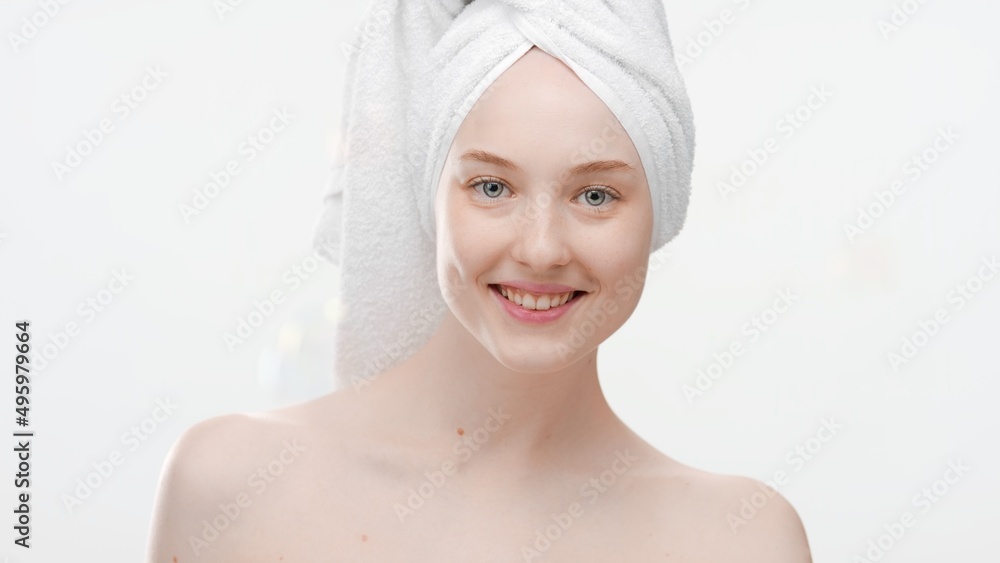 Beauty portrait of young positive Caucasian woman with a towel on her hair who smiles for camera on white background | After shower skin care commercial concept Beauty portrait of young positive Caucasian woman with a towel on her hair who smiles for camera on white background | After shower skin care commercial concept