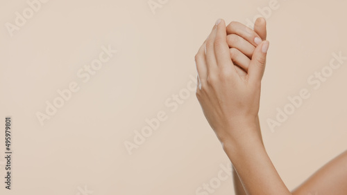 Horizontal close-up shot of female hands are rubbed and interlocked on beige background | Hand care concept