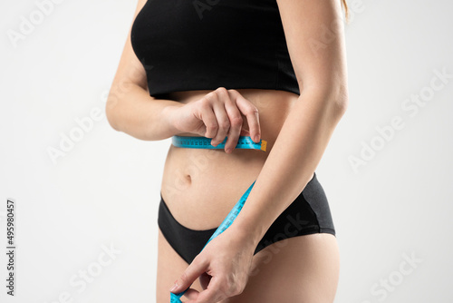 Fitness woman in a black underwear holding measuring tape around her waist isolated over white background.