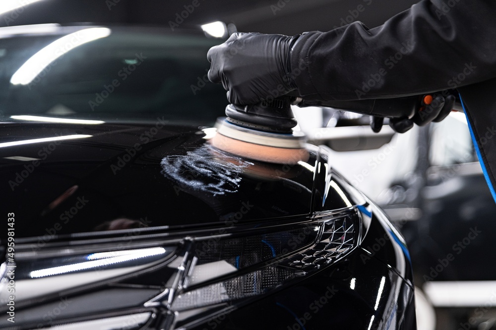 Man worker of car detailing studio removing scratches on car varnish with eletric polisher