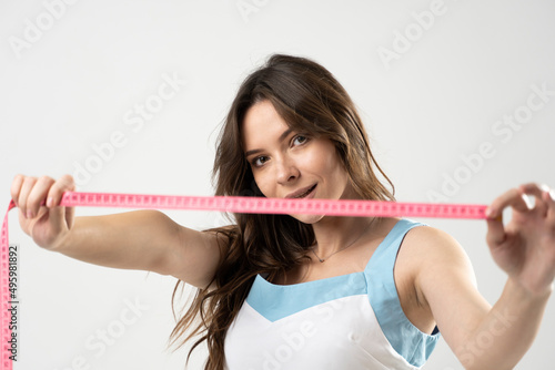 Attractive sexy brunette woman with slim body looking in a camera and showing a pink centimeter tape. Healthy lifestyles concept. Sport and diet. © Volodymyr