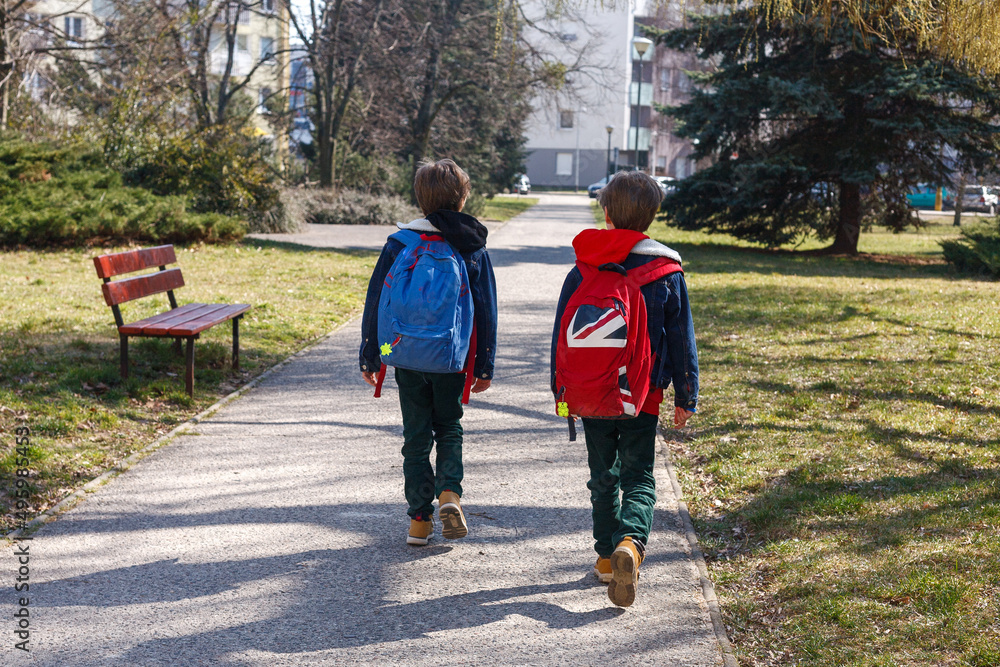 Two children walking with backpacks to school along an alley housing estate - obrazy, fototapety, plakaty 