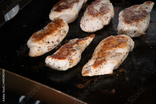 Marinated chicken breast cooking on an outdoor griddle with steam rising. photo