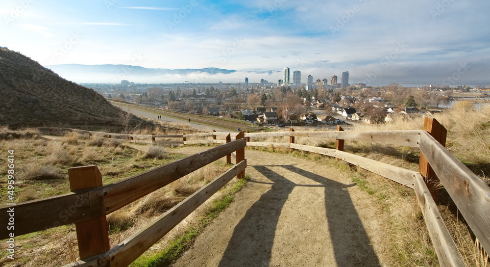View down a mountain pathway overlooking a city, as bright sunlight crests the mountain, making crisp shadows on the ground.