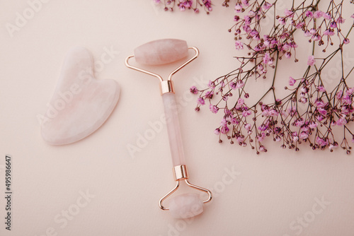 Face roller and gua sha massager on a pink background with gypsophila. Self facial massage concept photo