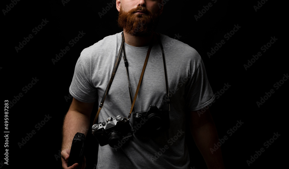 Professional photographer in a grey t-shirt with a bunch of different cameras on a shoulder.