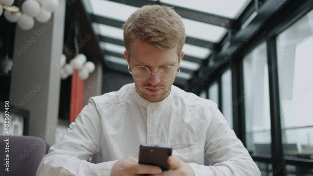 handsome caucasian man with eyeglasses is using smartphone for chatting and sending email, sitting alone in cafe handsome caucasian man with eyeglasses is using smartphone for chatting and sending email, sitting alone in cafe