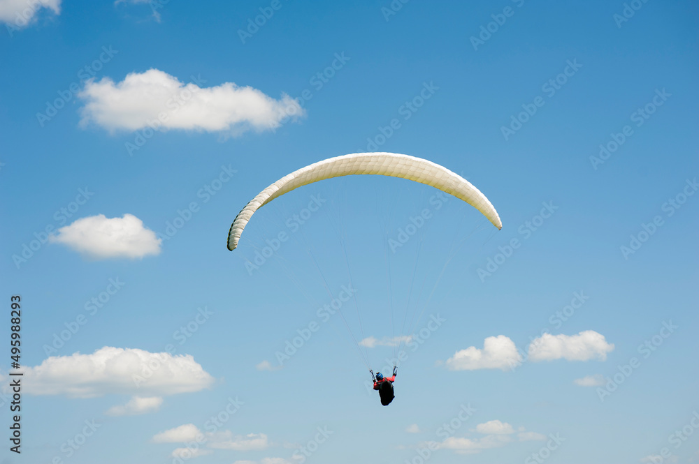 Alone white paraglider flying in the blue sky against the background of clouds. Paragliding in the sky on a sunny day. Alone white paraglider flying in the blue sky against the background of clouds. Paragliding in the sky on a sunny day.
