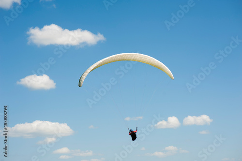 Alone white paraglider flying in the blue sky against the background of clouds. Paragliding in the sky on a sunny day.