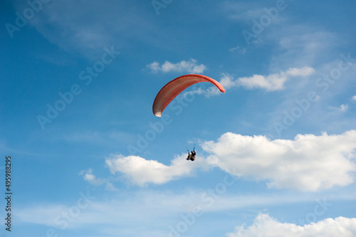 Alone red paraglider flying in the blue sky against the background of clouds. Paragliding in the sky on a sunny day.