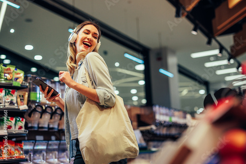 Tableau sur toile Joyful woman with earphones listening to the music in a supermarket