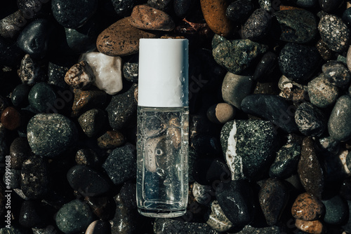 Flat lay composition of a beauty product transparent bottle on wet beach stones . Fresh ocean scented product mock up. 