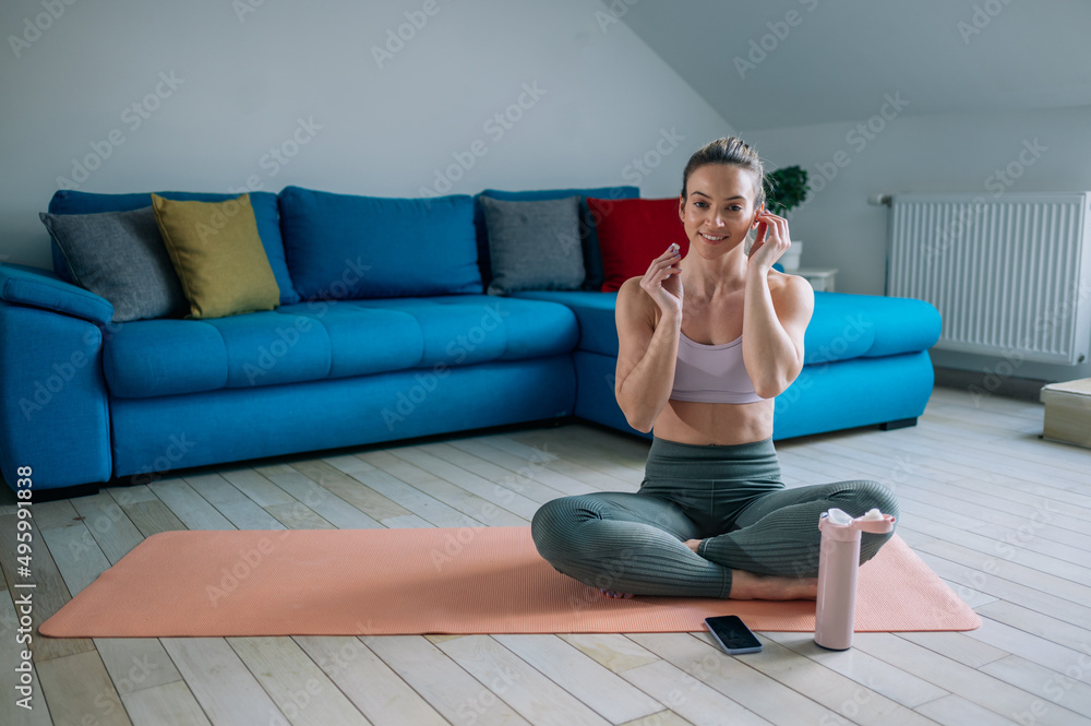 Obraz premium Woman using airpods and a smartphone while training at home