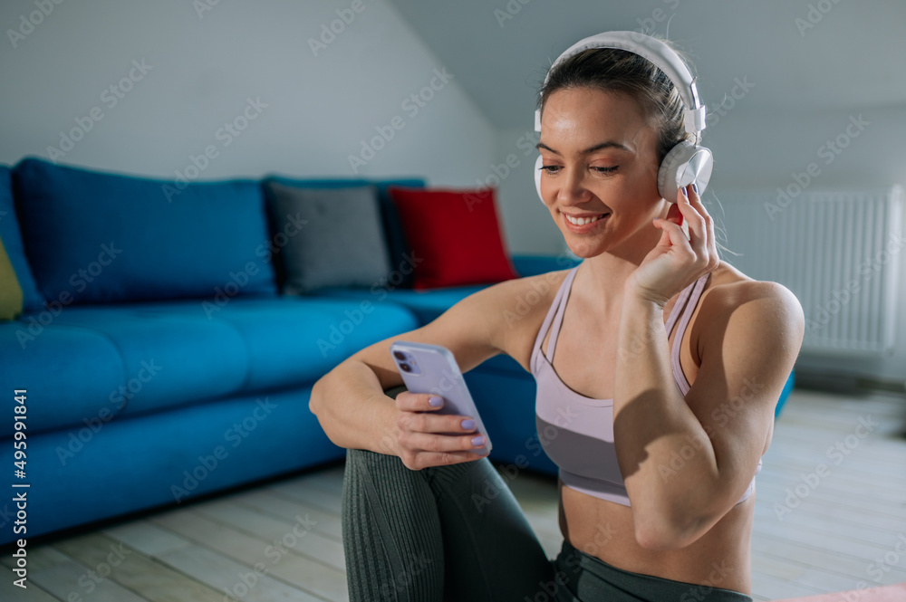 Woman using headphones and a smartphone while training at home Woman using headphones and a smartphone while training at home
