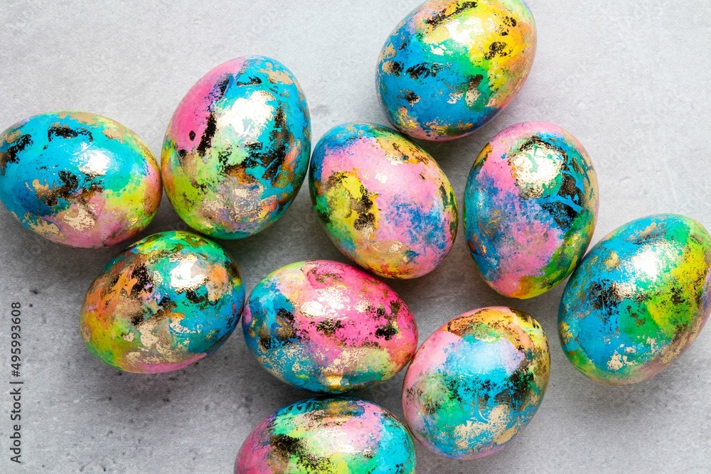 Happy Easter holiday greeting card with gold, blue, yellow, pink painted speckled easter eggs on grey background. Top view. Happy Easter holiday greeting card with gold, blue, yellow, pink painted speckled easter eggs on grey background. Top view.