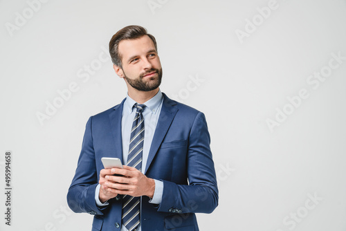 Pensive thoughtful caucasian young businessman ceo boss contemplating using smart phone cellphone for e-banking, e-learning, e-commerce isolated in white