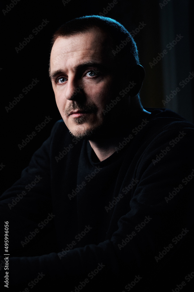 Profile portrait of a concentrated guy in a black jacket, in a dark room. Serious look. Blue eyes
