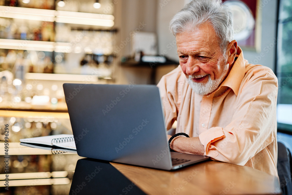 A senior student is sitting in the cafeteria and following online lectures with attention on his laptop. A senior student is sitting in the cafeteria and following online lectures with attention on his laptop.