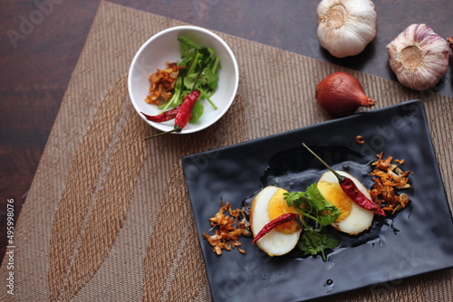 Egg with Tamarind Sauce in a white plate served on a wooden table with coriander sprinkles, is a popular local dish that Thai people eat.