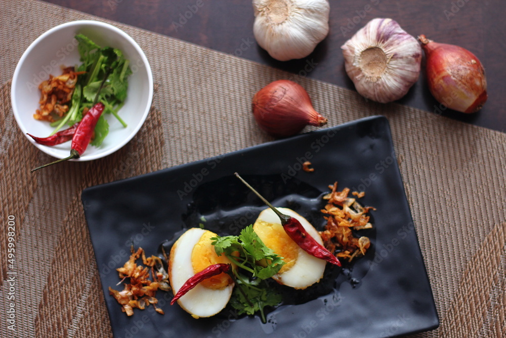 Egg with Tamarind Sauce in a white plate served on a wooden table with coriander sprinkles, is a popular local dish that Thai people eat. Egg with Tamarind Sauce in a white plate served on a wooden table with coriander sprinkles, is a popular local dish that Thai people eat.