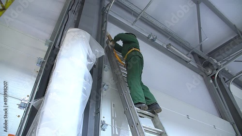 Professional worker climbing up ladder indoors to repair a transformer. Man in a workwear