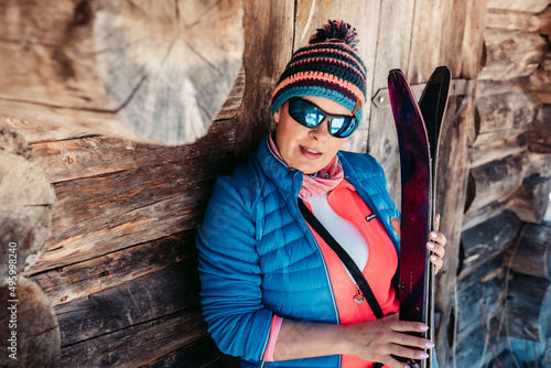 Kobieta szczęśliwa z nartami w zimowy dzień pozuje przy starej stodole.