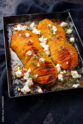 Traditional fried hasselback butternut squash pumpkin roast with herbs and feta sheep cheese served as top view in a rustic metal tray on an old black board