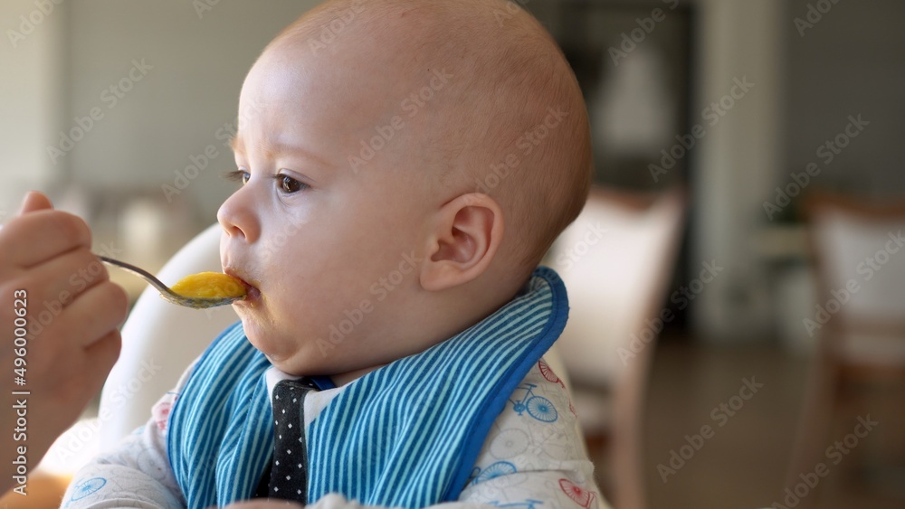mom Mother feed young baby in white feeding up high chair, first supplement vegetable puree Happy smiling kid eat for the frst time, child with dirty face, little infant boy eating porridge nutrition mom Mother feed young baby in white feeding up high chair, first supplement vegetable puree Happy smiling kid eat for the frst time, child with dirty face, little infant boy eating porridge nutrition