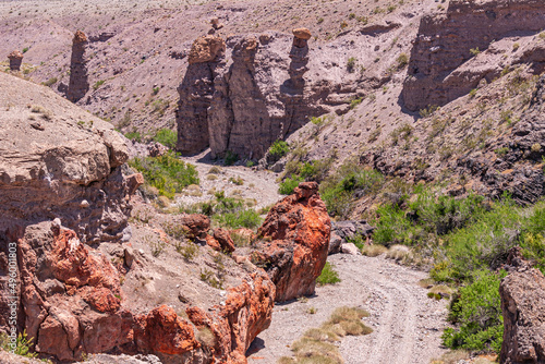Nelson, Nevada, USA - May 21, 2011: Geologic pillars with golden crowns along dirt road in Eldorado canyon and mountains. Red rocks and green weeds add colors.