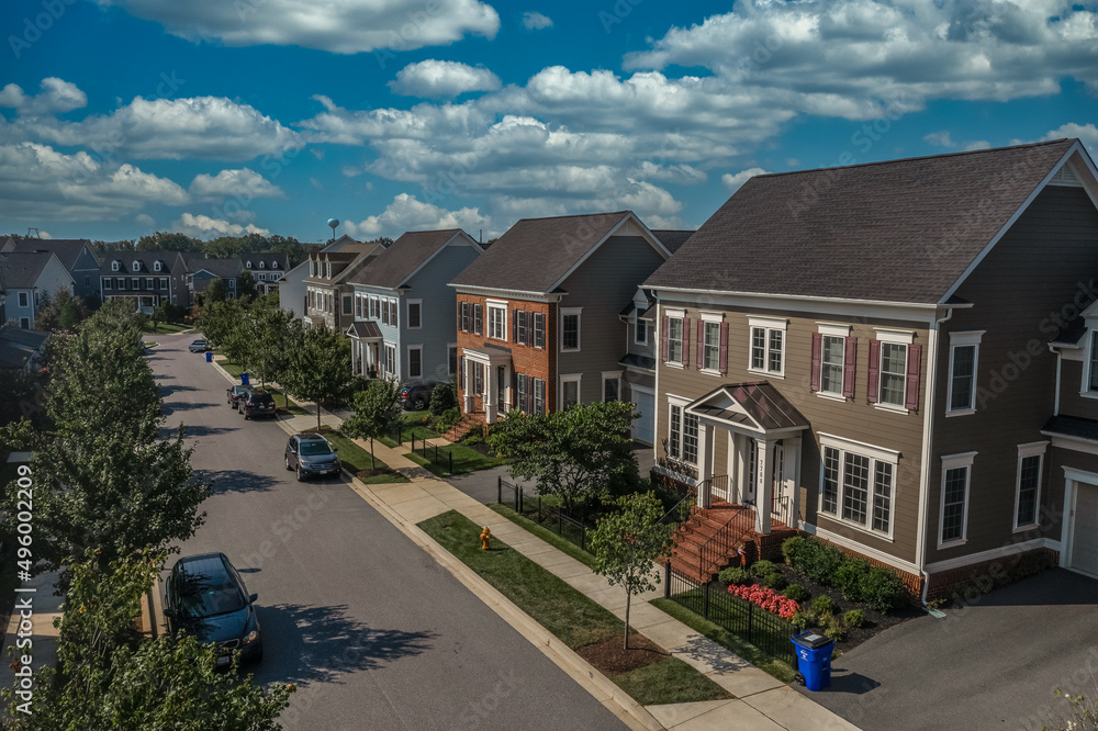 Aerial view of modern upper class suburban American real estate development community, large single family homes with vinyl and brick siding portico leading up to the entrance cloudy blue sky
