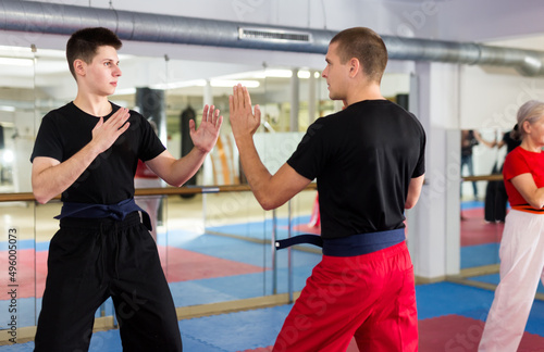Focused young guy in black sportswear sparring with experienced martial arts trainer during training in gym