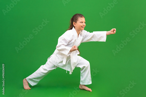 A young girl trains in karate. Isolated on a green background,